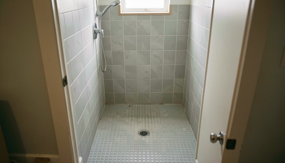 Step-free walk-in shower with light grey non-slip floor tile and a handheld shower head in a small renovated bathroom